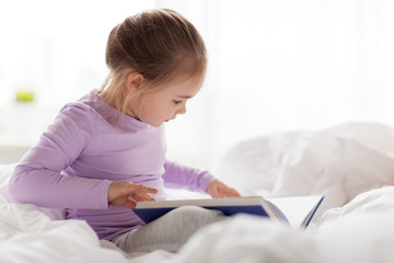 happy little girl reading book in bed at home