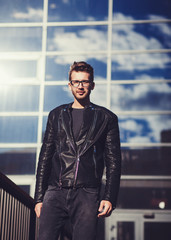 High fashion look.Young stylish handsome man model in leather jacket lifestyle in the street in glasses