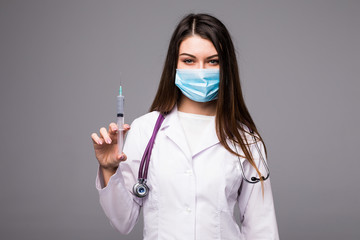 Doctor or nurse in face mask and lab coat holding syringe. Isolated over grey
