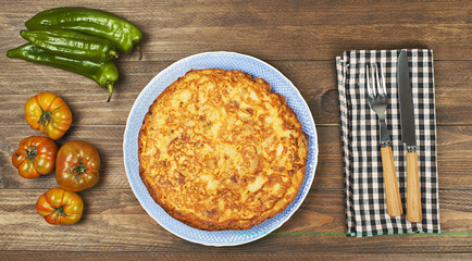 From above typical Spanish omelette with tomatoes, green peppers and oil in bottle on wooden table.