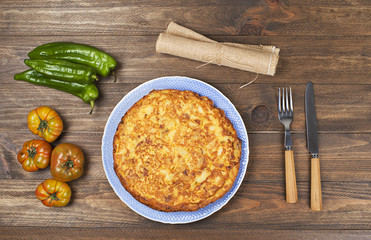 From above typical Spanish omelette with tomatoes, green peppers and oil in bottle on wooden table.