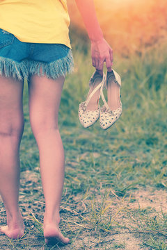 Young woman walking barefoot and carrying high heels