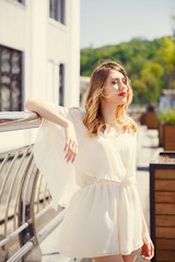 Portrait of a young girl in a light dress on a background of a sunny city