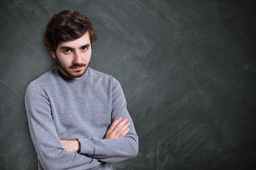 A portrait of serious young bearded guy with stylish hairstyle dressed in casual sweater standing crossed hands looking serious and confident.
