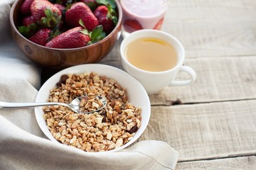 Obraz na płótnie Canvas A bowl of homemade granola with yogurt and fresh strawberries on a wooden background. Healthy breakfast with green tea