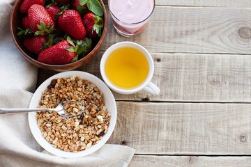 A bowl of homemade granola with yogurt and fresh strawberries on a wooden background. Healthy breakfast with green tea