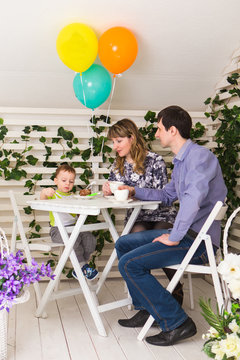 family, parenthood, happy birthday and holiday concept - happy parents and child at a table drinking tea and eating cake.