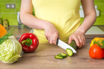 Woman cutting cucumber for salad - fresh vegetables concept