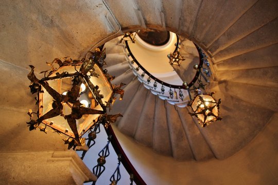 Spiral staircase in an old building, with wrought iron railings and lamps. Italy, Europe.