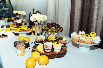 Holiday candy bar in yellow and brown color. Wedding candy bar served with cupcakes, cake pops, desserts in glasses, lemons and coffee beans