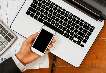 hand holding smartphone with laptop and office tools