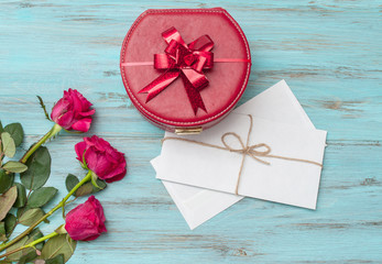 Roses and a box with a gift on a turquoise wooden background. Top view with space for text.
