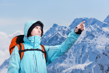 The mountaineer pointing at peak, standing against a winter mountain landscape.