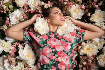 Sensual woman lying down on flowers in studio photo. Beauty concept. Floral decoration
