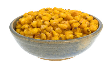 Toasted corn nuts in an old stoneware bowl isolated on a white background.