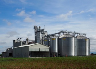 Grain storage bins under blue sky with clouds