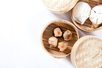 Dim sum and steamed buns in bamboo steamer on white background