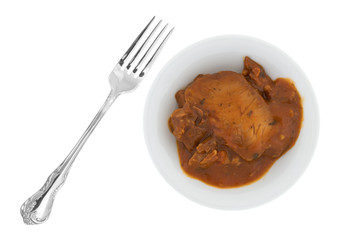 Top view of a bowl of tilapia fillets in marinara sauce plus a fork to the side isolated on a white background.