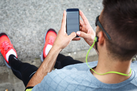 Man relaxing after jogging.He using his smart phone and listening to music.