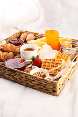 breakfast in bed with fruits and pastries on a tray -waffles, croissants, coffe and juice