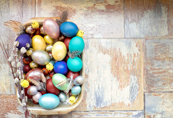 On the old wooden shabby table a dish of metal with painted in different colors Easter eggs with feathers willow and chickens
