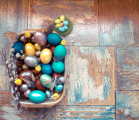 On the old wooden shabby table a dish of metal with painted in different colors Easter eggs with feathers willow and chickens