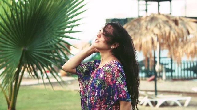 young tanned woman with long hair under tropical palm trees in summer. slow motion