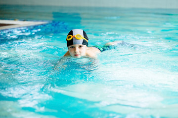 Little cute boy learning to swim in sport pool. Swimming school for small children. Healthy kid enjoying active lifestyle.