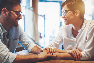 Obraz premium Young couple in love holding hands, looking at each other and smiling while sitting at cafe