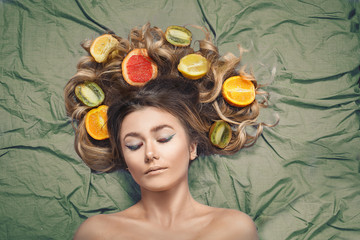 Beautiful gorgeous model girl with colorful citrus healthy fruits in her shiny hair. Care and hair...