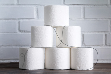 Stack of toilet paper rolls on wooden table against white brick wall. Copy space.