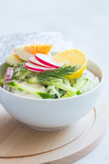 Vegetable salad with yogurt dressing with eggs in a white bowl on wooden board. Various vegetables in a white bowl on wooden board. Healthy summer snack. Clean eating.