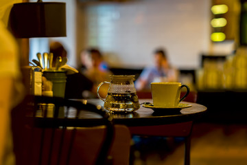 Cup of coffee, glass teapot of hot water, cafe in the morning. Image with blur in low key, for background use. Concept lifestyle