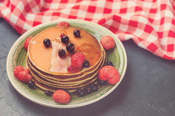 Stack of pancakes with frozen berries and honey on black background. Selective focus. Toned.
