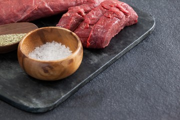 Beef steak, salt and spices on black slate plate