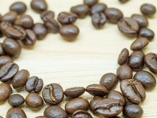 The group of thin coffee beans is on light wood background.