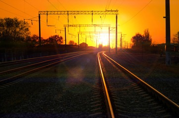 Fototapeta na wymiar Railway - Railroad at sunset with sun, Rails and electric lines in yellow light