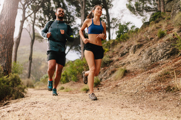 Fit young couple running on mountain trail in morning