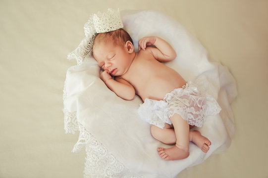 Adorable beautiful newborn baby girl with a crown on the head. One week old newborn baby sleeping in basket.