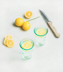 Morning detox lemon water in glasses and fresh lemons over light grey marble background, selective focus. Clean eating, weight loss, healthy, detox, dieting concept