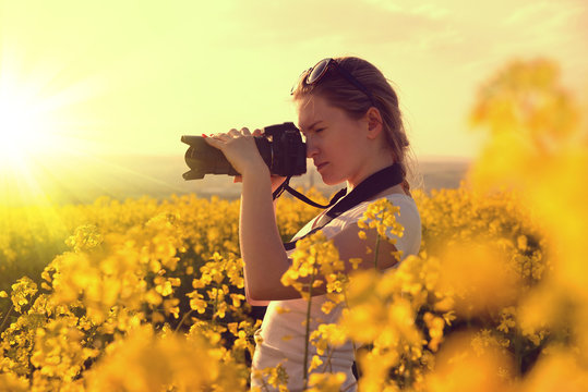 Woman making photos of rapeseed field with digital camera at sunset.