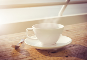 cup of coffee on wooden table with morning sun vintage effect