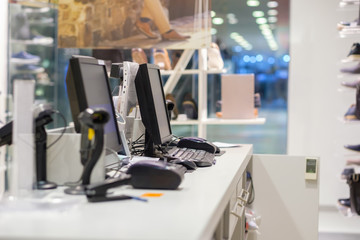 Two cash desks with computer screens and barcode scanners on white table and wall in small store