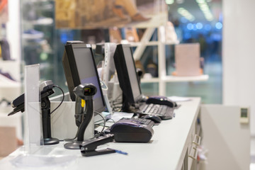 Two cash desks with computer screens and barcode scanners on white table and wall in small store