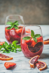 Blood orange and strawberry summer Sangria. Fruit refreshing rose wine cocktails in glasses with ice and mint leaves on marble table, dark background, vertical composition, copy space
