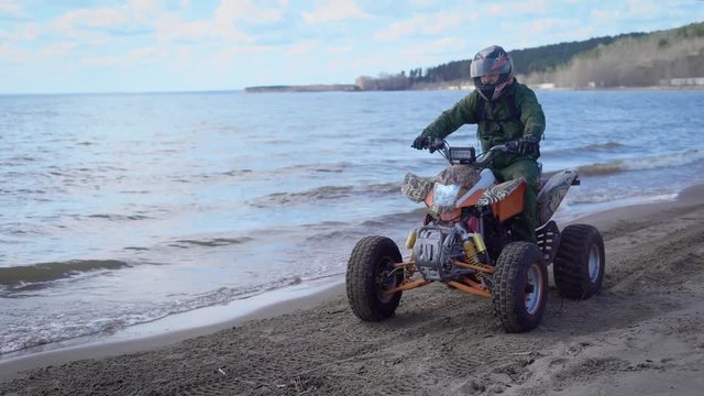 A young man is riding along the beach line near the sea on a sport quad bike with a lightweight body for a more speedy ride