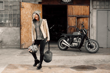 Young woman near a garage. A woman in a leather jacket. Motorcycle near the garage.