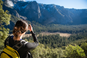 Female tourist take a photograping of Yosemite Valley with pine forest in foreground sun light lay on the forest