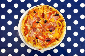Pizza with sausage and olives on a blue surface with white circles. top view.