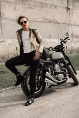 Obraz na płótnie Canvas Woman sitting on his motorcycle. Motorcycle near a grey wall. girl with short hair. girl in black glasses and a leather jacket. Bike